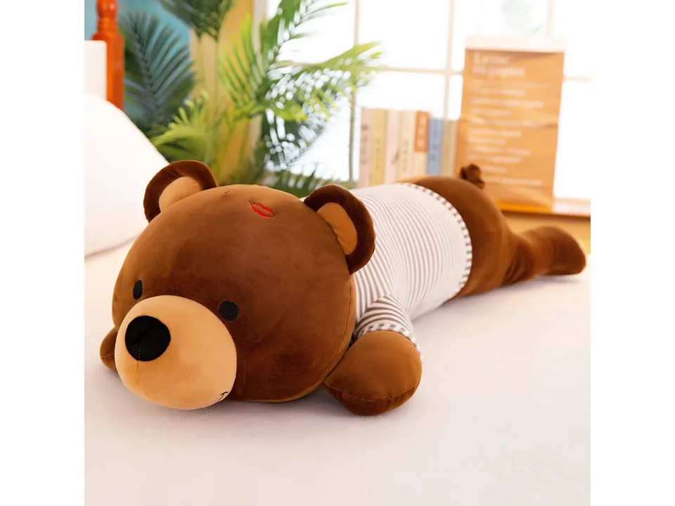 A brown plush bear toy with a striped shirt lying on a bed.