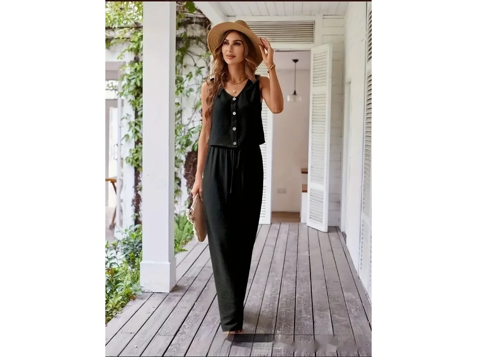 A woman wearing a black sleeveless vest and matching wide-leg pants, standing on a porch.