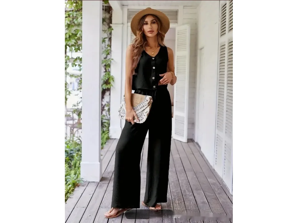 A woman wearing a black vest and wide-leg pants, holding a woven clutch bag.