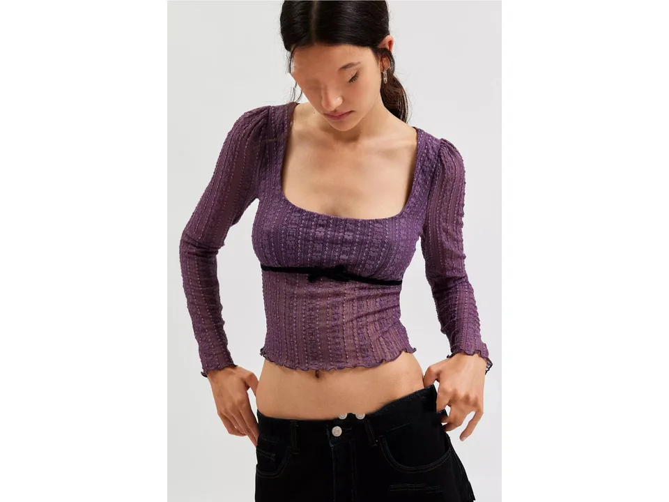 A model wearing a purple long sleeve lace mesh top with a black bow detail.