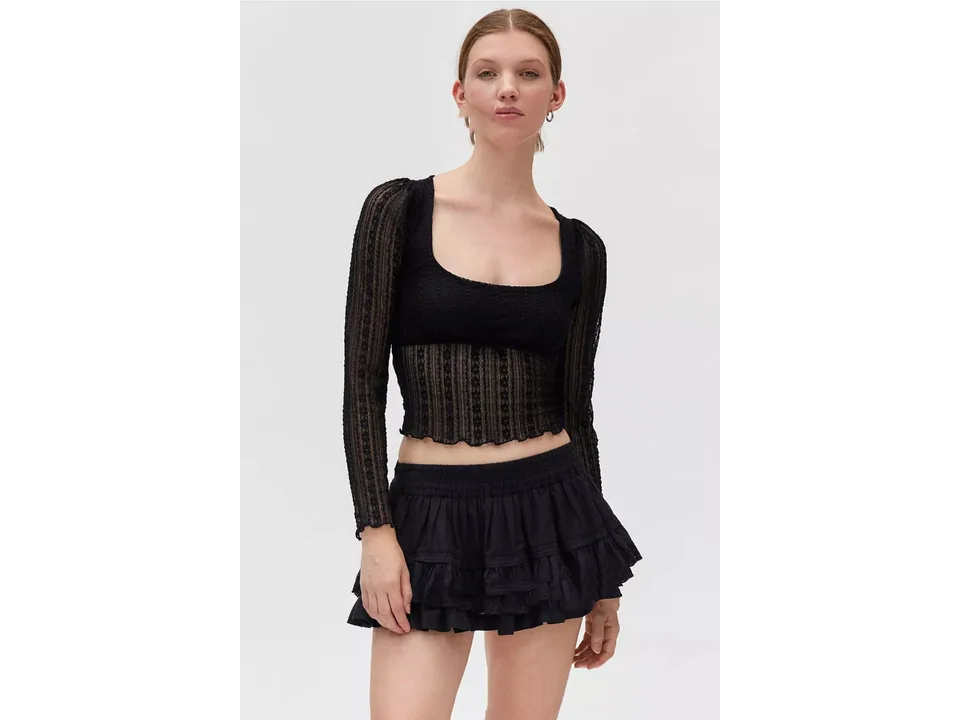 A model wearing a black long sleeve lace mesh top with a ruffled skirt.