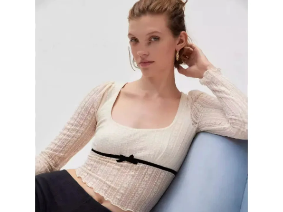 A model wearing a cream-colored long sleeve lace mesh top with a black bow detail.