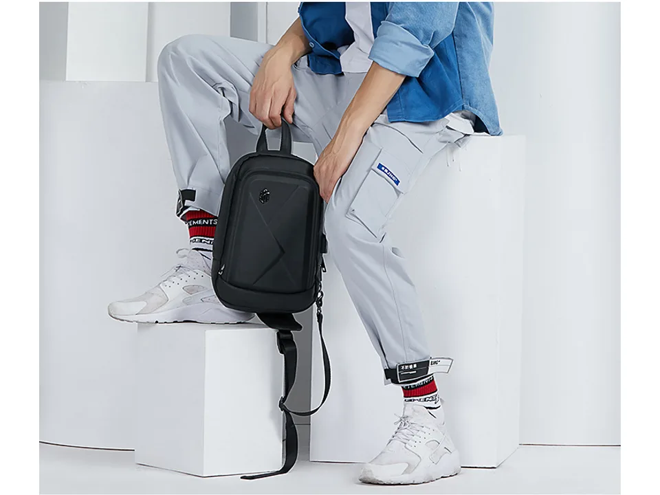 A person sitting while holding the black chest bag.