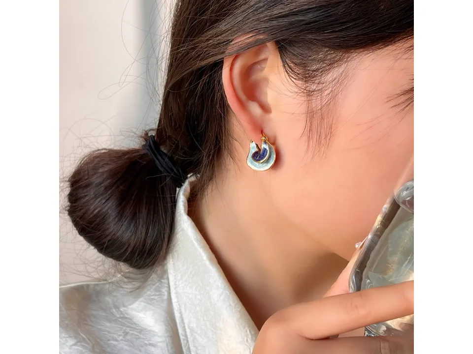 A woman wearing the blue and gold spiral hoop earrings.