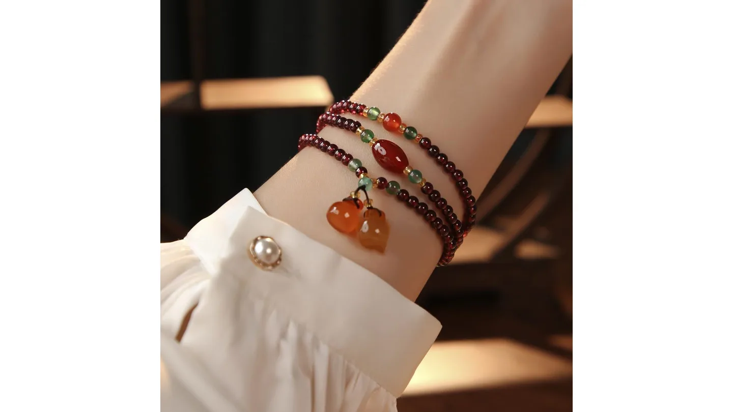 A garnet beaded bracelet with agate charms worn on a wrist.