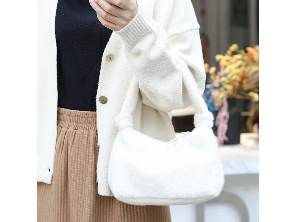 A person holding a white furry mini handbag.