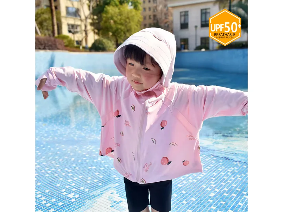 A child wearing a pink peach-patterned sun jacket with a hood by a pool.