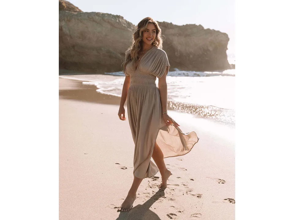 Model walking on the beach in a beige maxi dress, showing the flowy skirt and slit.
