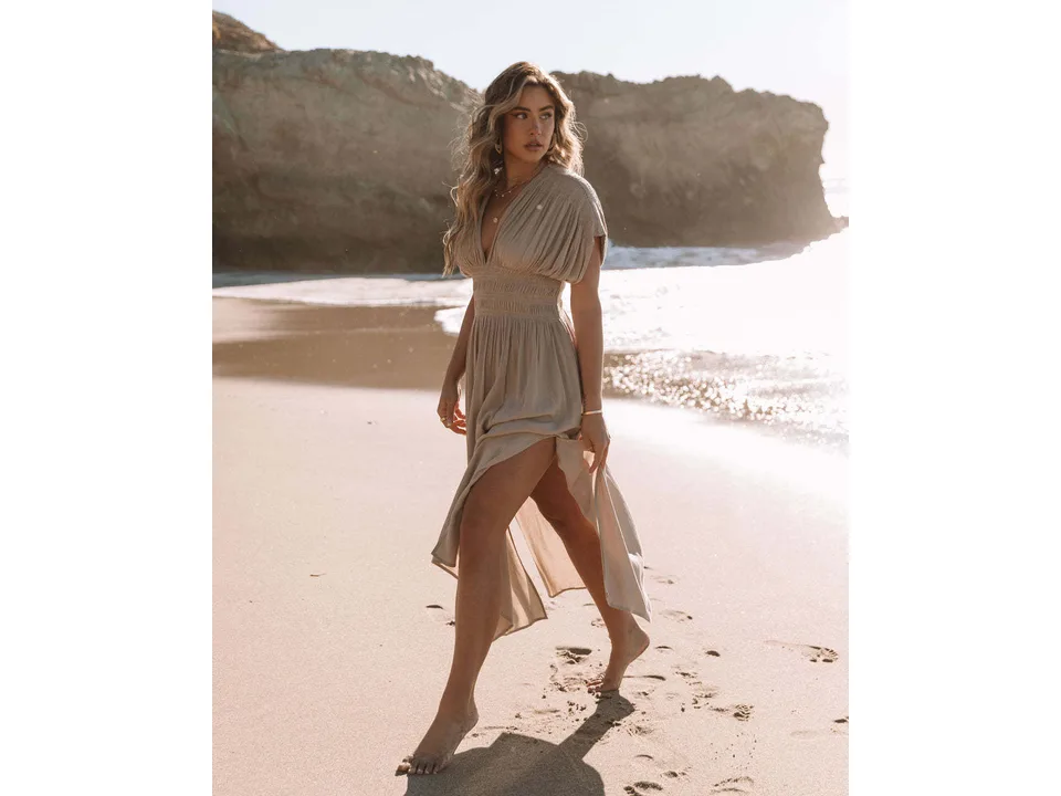 Model walking on the beach wearing a beige maxi dress with a V-neck.