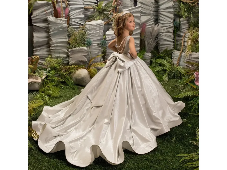 Back view of a girl wearing a silver formal dress with a large bow and long train.