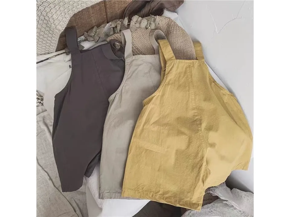 Three pairs of baby suspender shorts in yellow, beige, and dark grey laid out.
