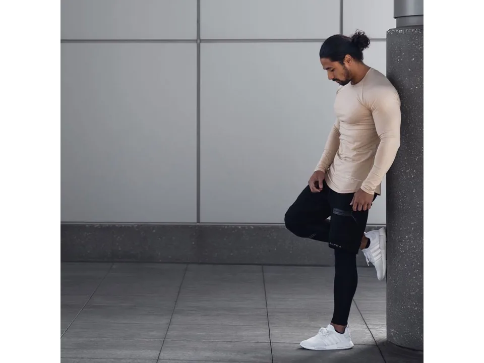 A man wearing athletic shorts and a long-sleeve shirt, leaning against a pillar.