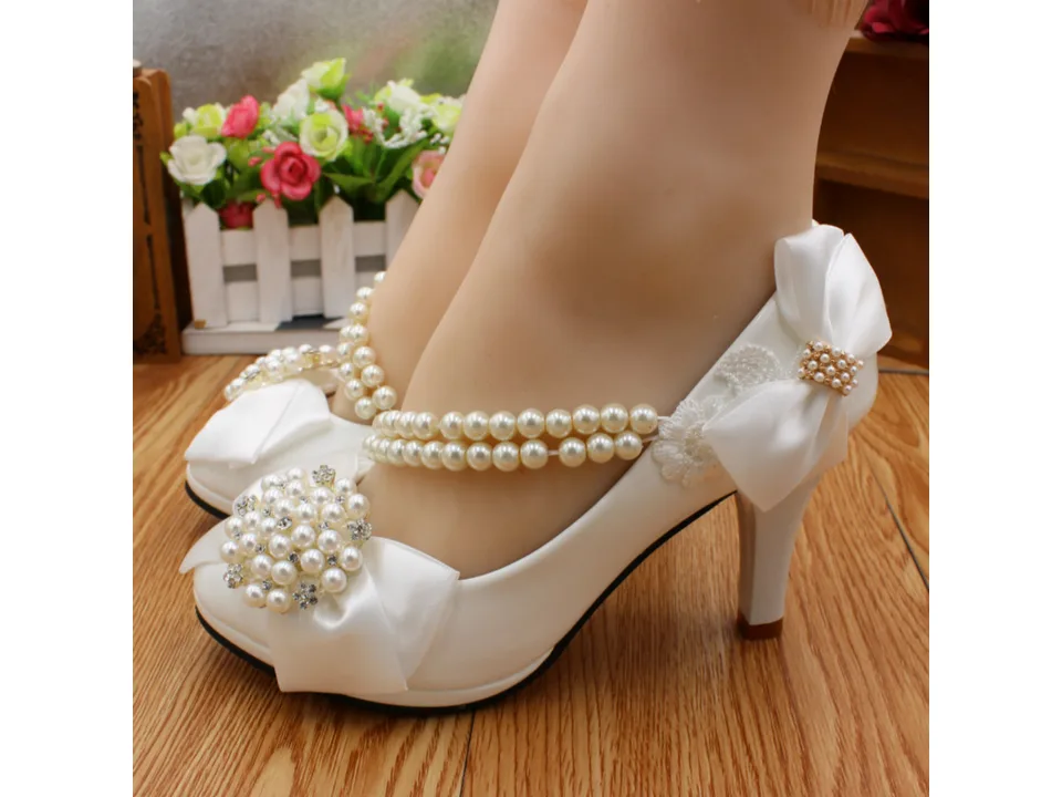 Side view of white bridal heels with pearl straps worn on a mannequin foot.