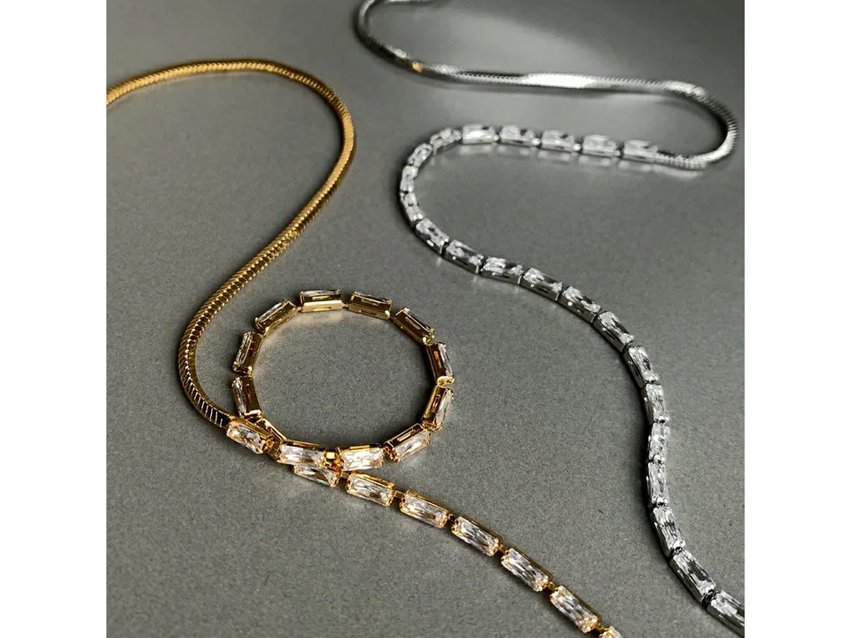 Gold and silver half chain and cubic zirconia necklaces laid out on a grey surface.