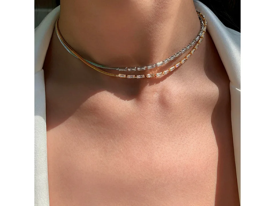 Close-up of two necklaces, one gold and one silver, worn around the neck.