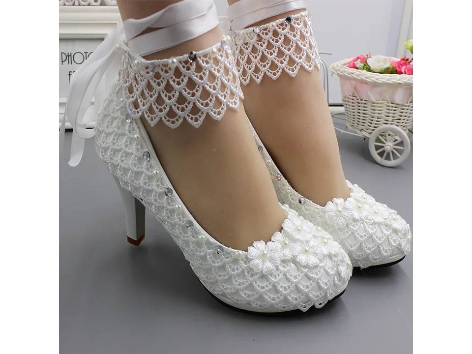 Side view of white lace wedding pumps with floral details and ankle ribbon.