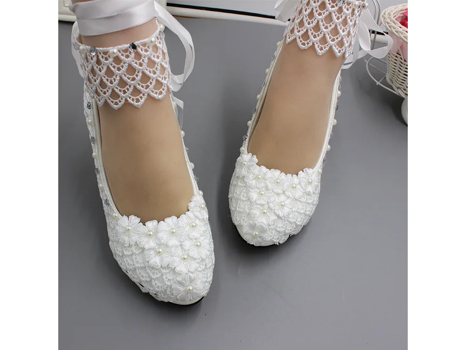 Front view of white lace wedding pumps with floral embellishments.