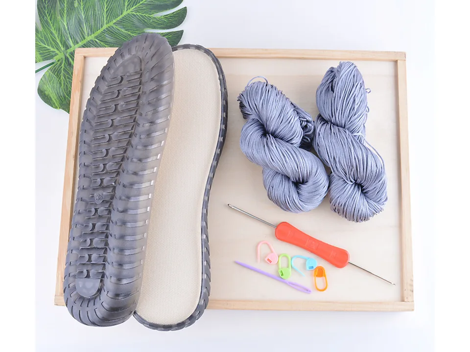 DIY crochet shoe kit including a black sole, grey yarn, crochet hook, and stitch markers.