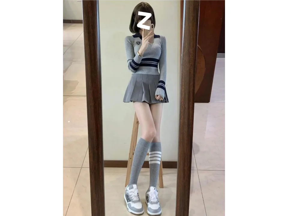 Full body view of the model wearing the knitted top, pleated skirt, and knee-high socks.