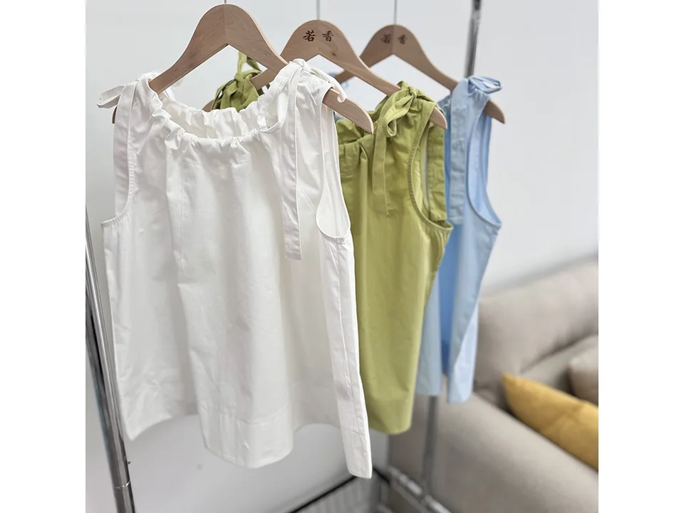 Three sleeveless cotton vests in white, light green, and light blue hanging on a rack.