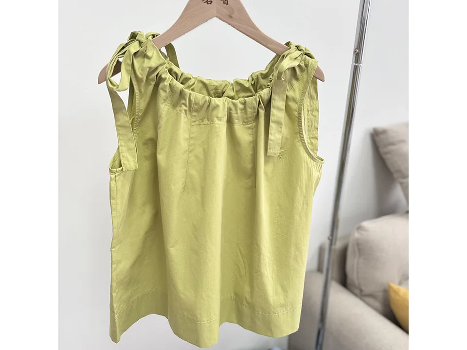 A light green sleeveless cotton vest with tie straps hanging on a wooden hanger.