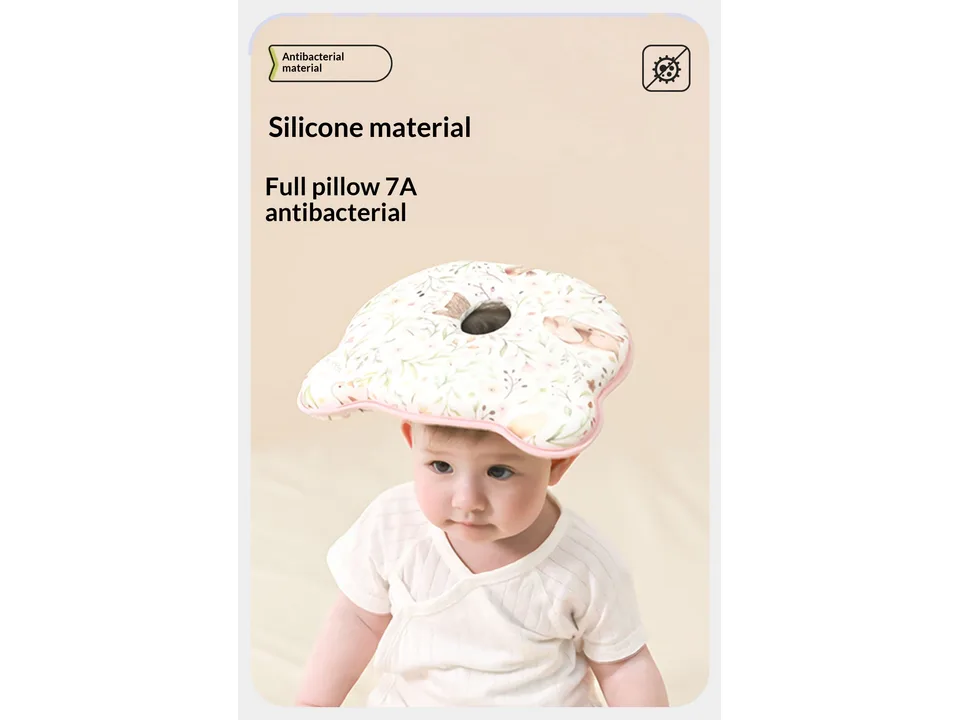 A baby sitting up with the head shaping pillow resting on their head.