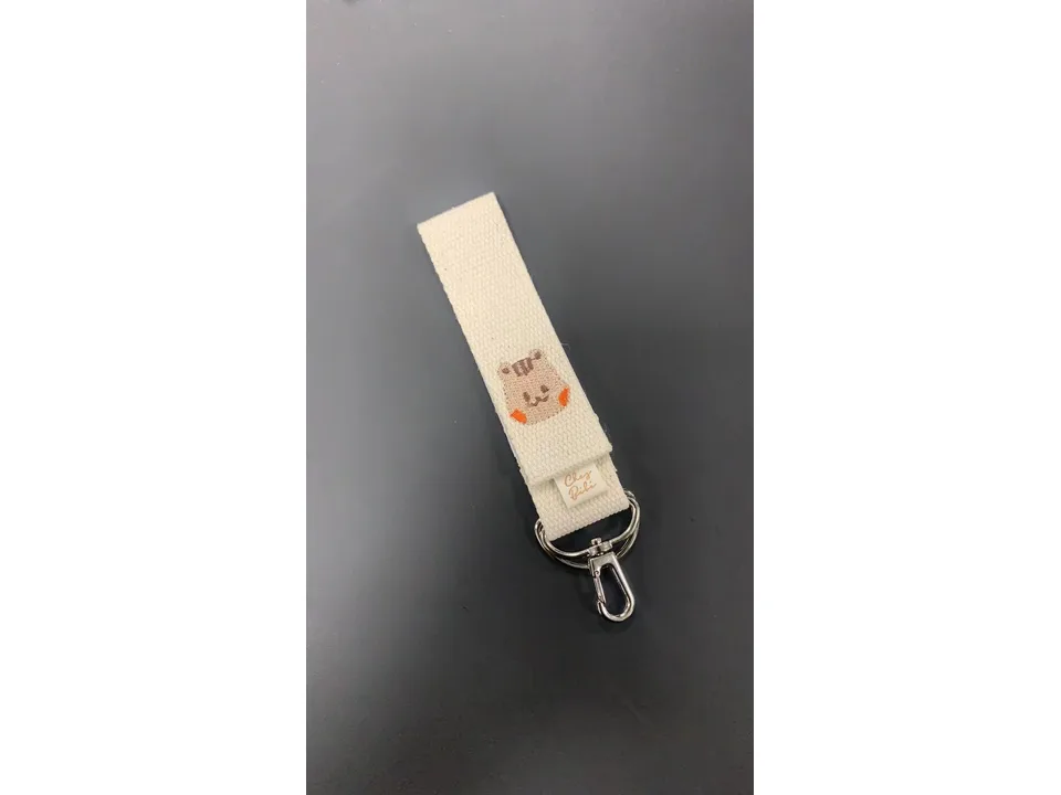 Close-up of a cream-colored fabric stroller hook with an embroidered hamster face.
