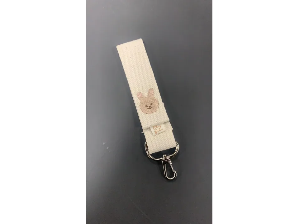 Close-up of a cream-colored fabric stroller hook with an embroidered bunny face.