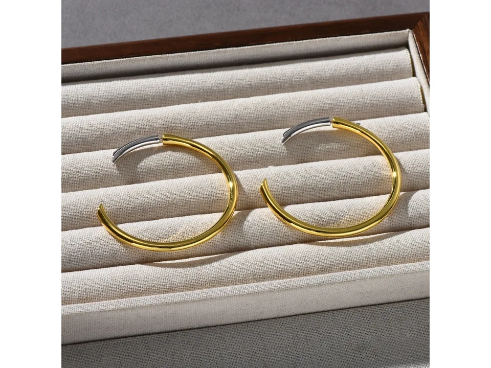 Two-tone hoop earrings with gold and silver sections resting in a jewelry display tray.