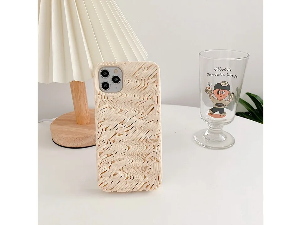Noodle-textured phone case standing on a table next to a lamp and a glass.