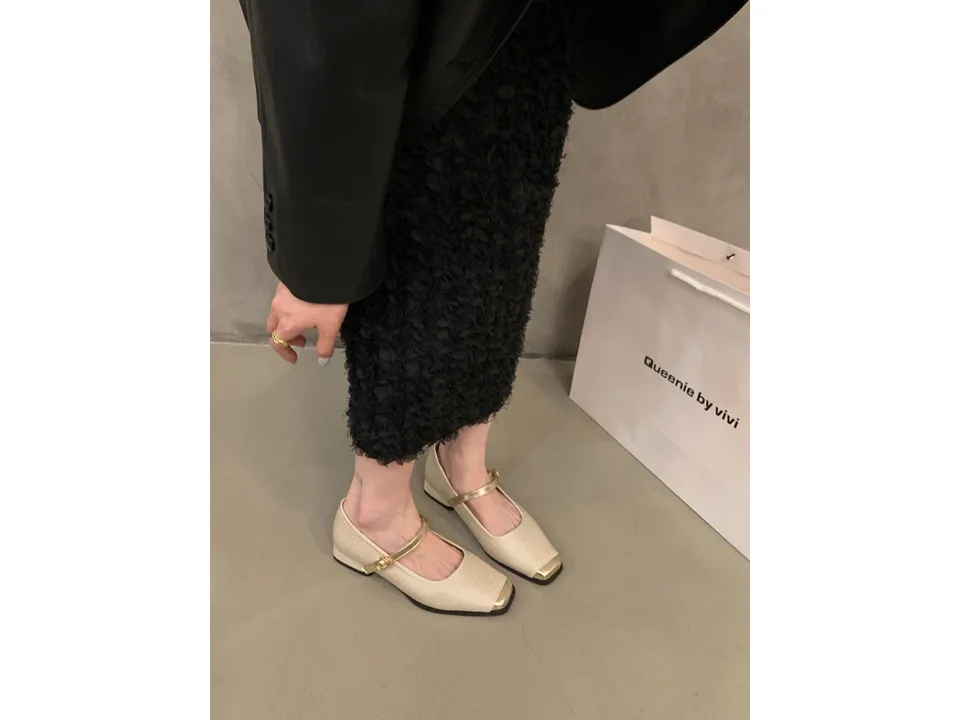 A person wearing beige Mary Jane pumps with a gold toe cap.