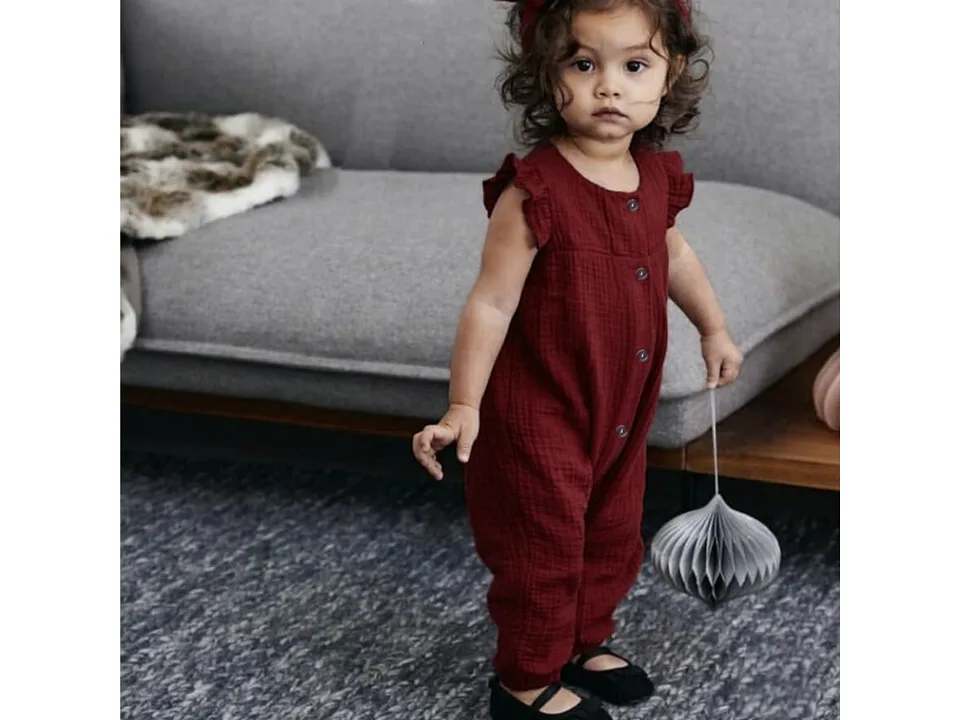 A young girl wearing a maroon cotton jumpsuit with ruffle sleeves.