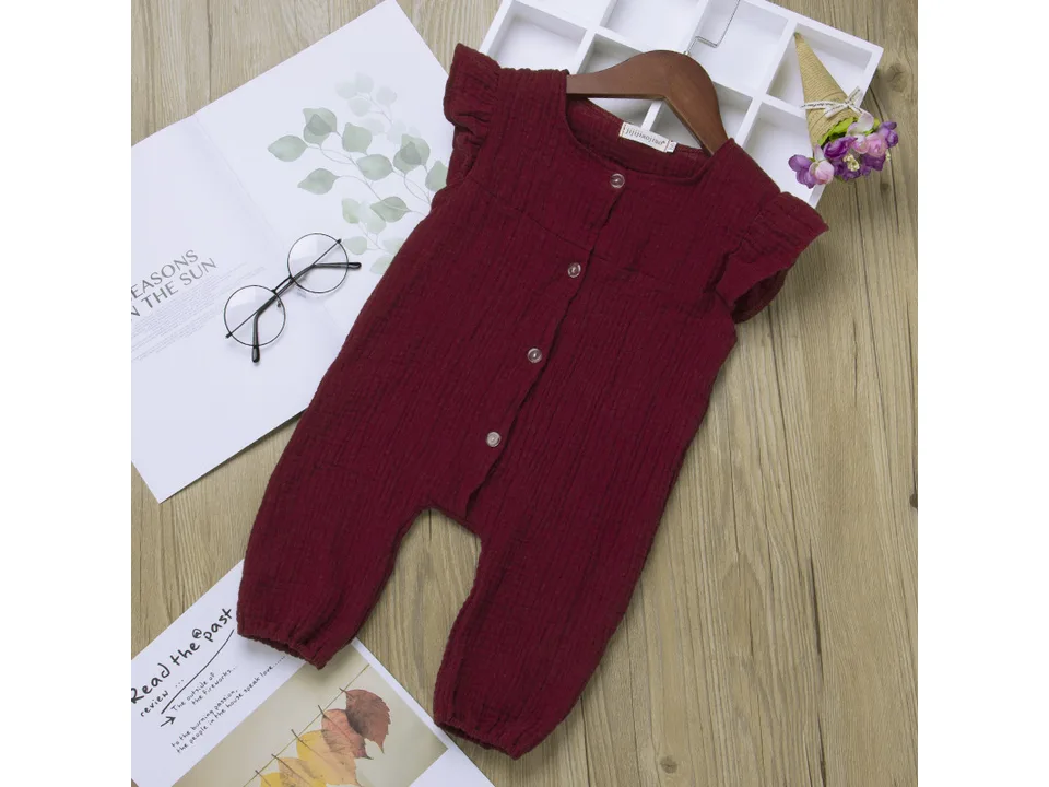 A maroon cotton jumpsuit with ruffle sleeves displayed on a wooden hanger.