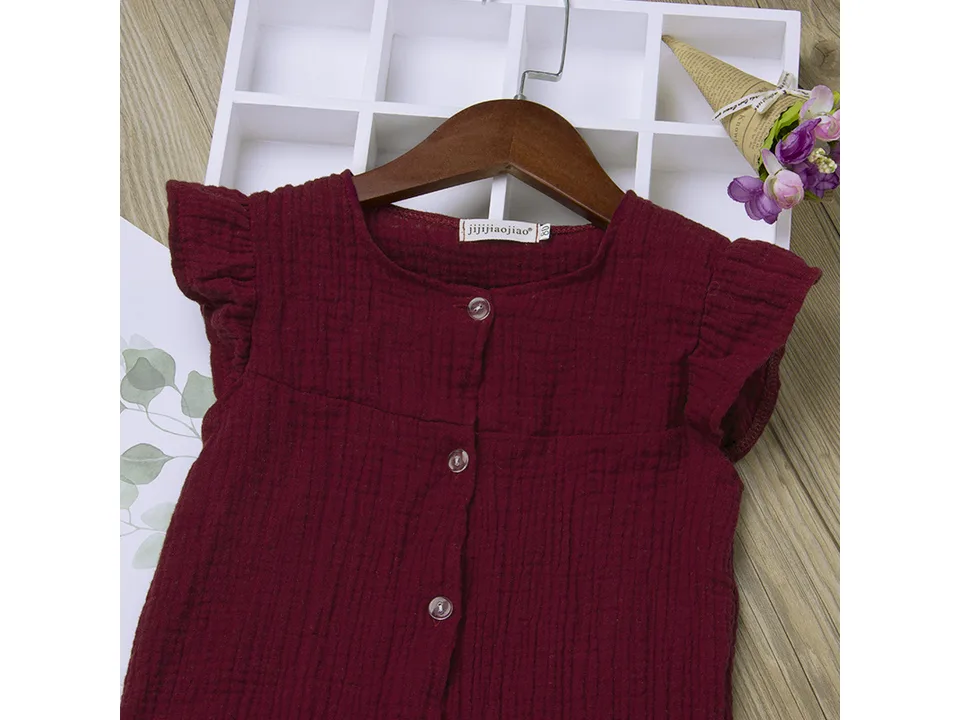 Close-up of the top of a maroon cotton jumpsuit showing buttons and ruffle sleeves.