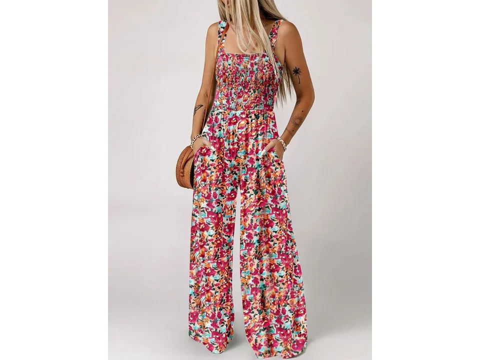 A woman wearing a colorful floral sleeveless jumpsuit with a smocked bodice and pockets.