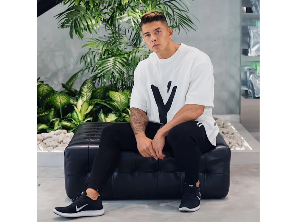 A man wearing an oversized white graphic t-shirt while sitting on a black leather bench.