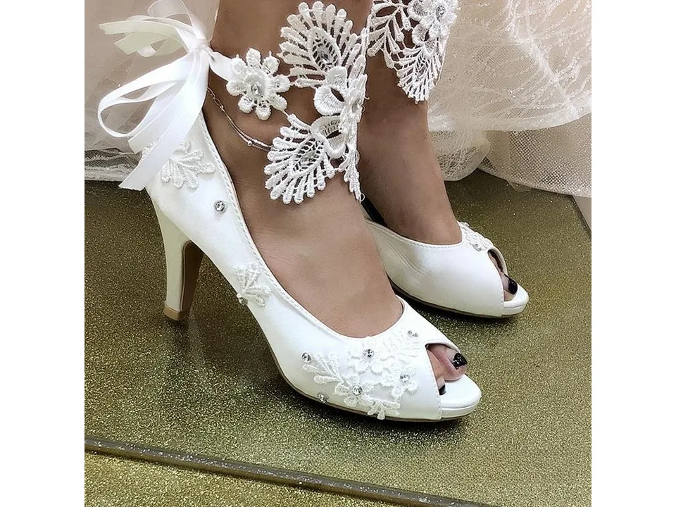 White lace wedding pumps worn on feet with decorative ankle lace.