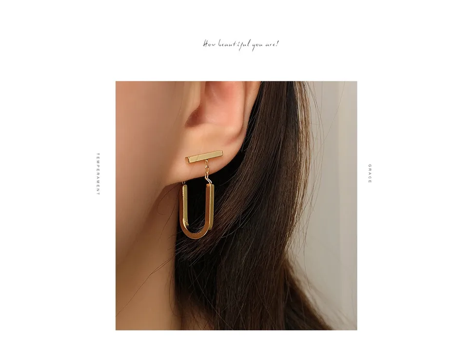A close-up view of a gold U-shaped drop earring worn on an ear.