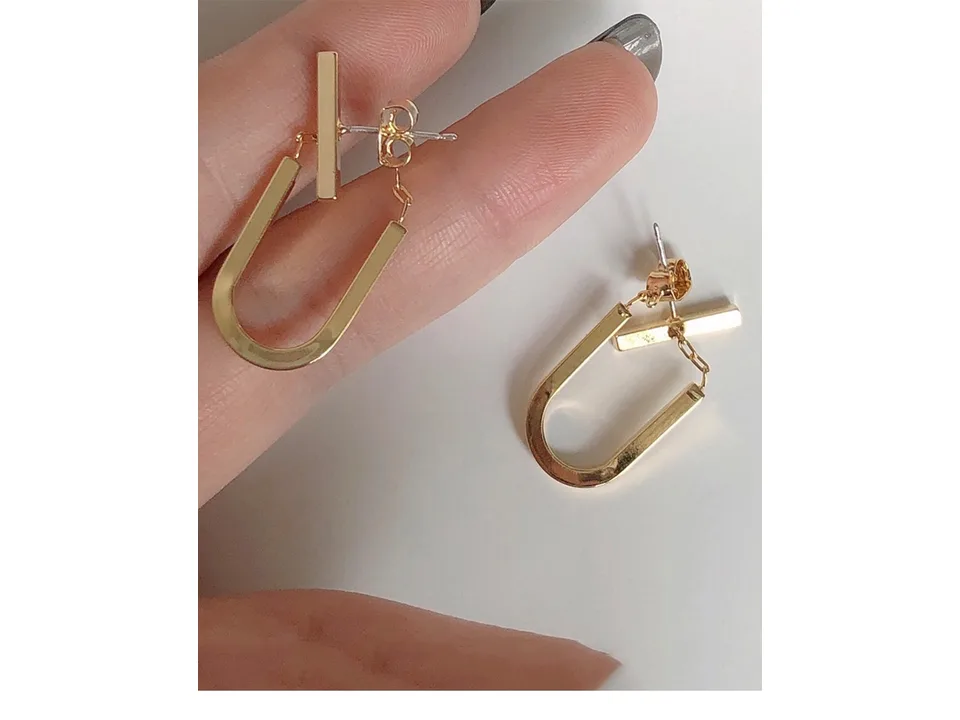 A close-up view of a pair of gold U-shaped drop earrings held in a hand.