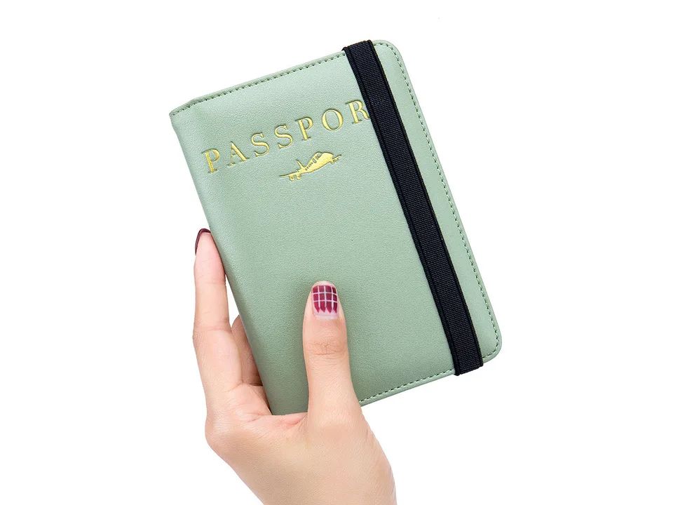 A hand holding a light green passport holder with an elastic strap.