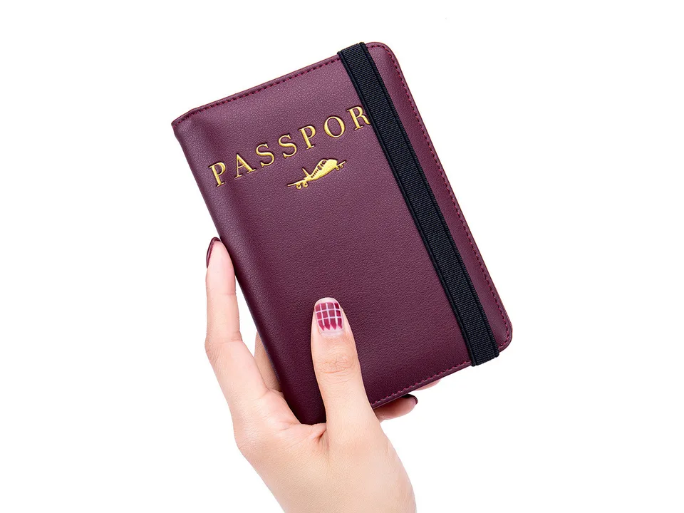 A hand holding a dark red passport holder with an elastic strap.
