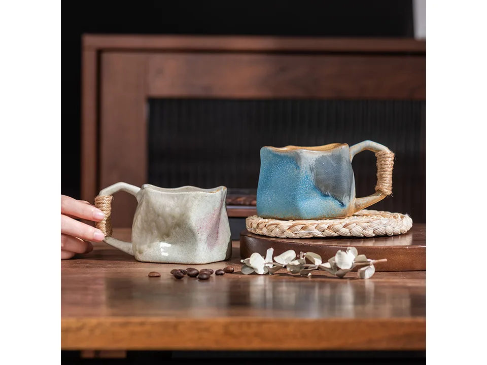 Two irregular ceramic mugs with rope handles sitting on a wooden surface.