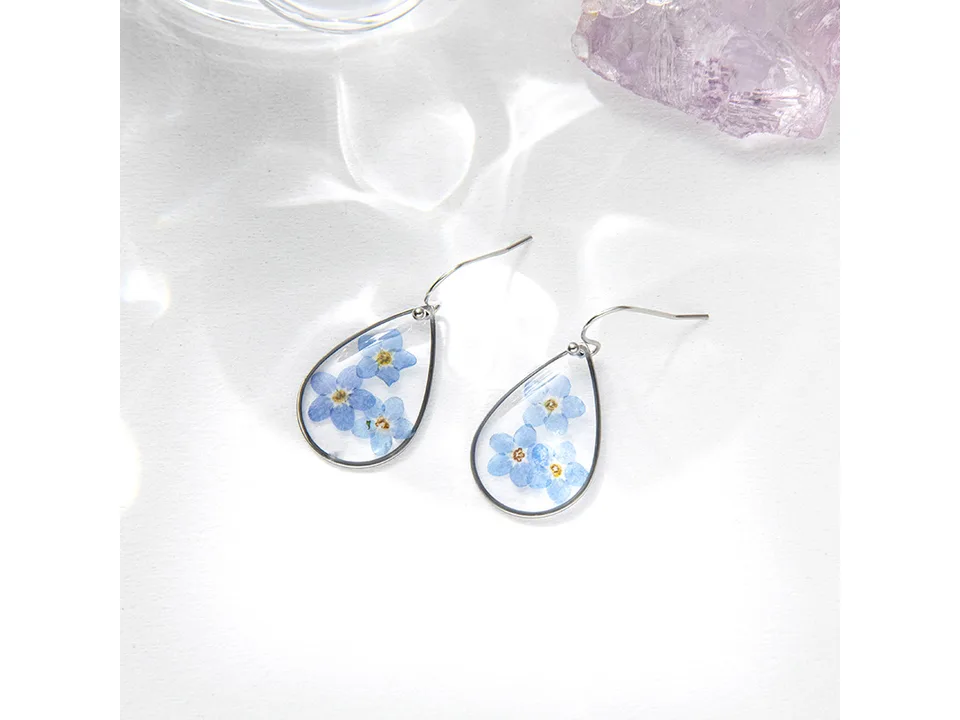 A pair of teardrop-shaped resin earrings with pressed blue flowers.