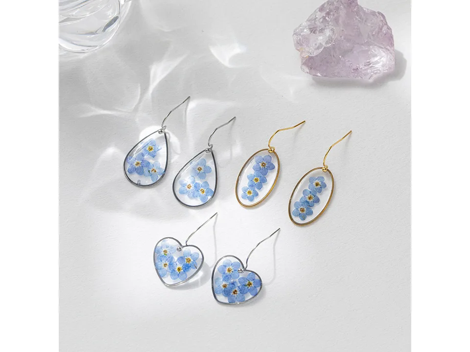Three pairs of resin earrings with pressed blue flowers in teardrop, oval, and heart shapes.