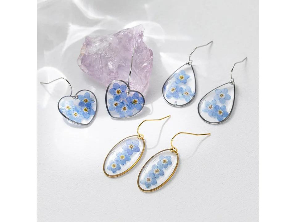 A collection of resin earrings featuring pressed blue flowers in heart, teardrop, and oval shapes.