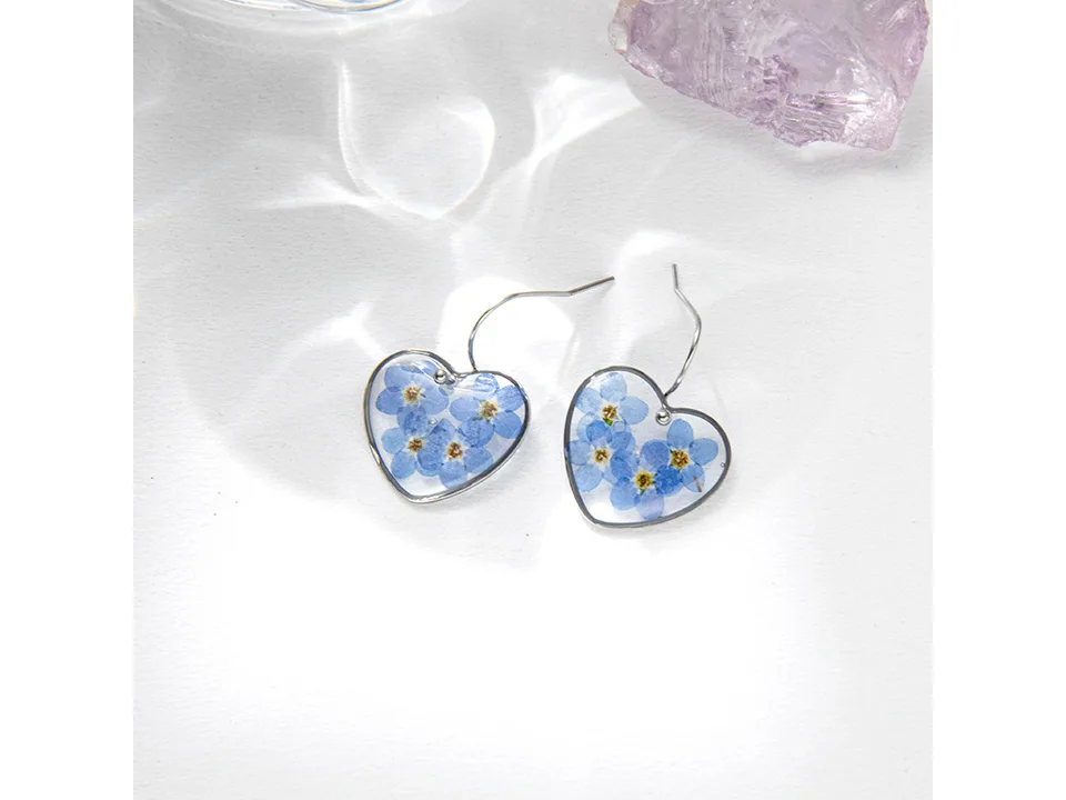 A pair of heart-shaped resin earrings with pressed blue flowers.