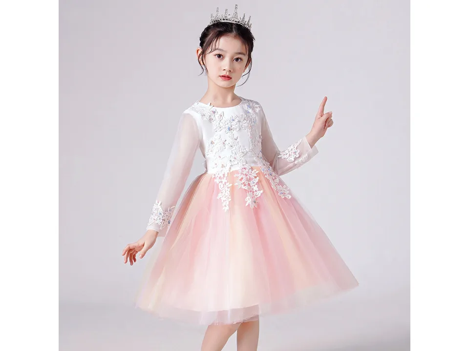 A young girl wearing a white long-sleeved dress with a rainbow gradient mesh skirt and floral lace bodice.
