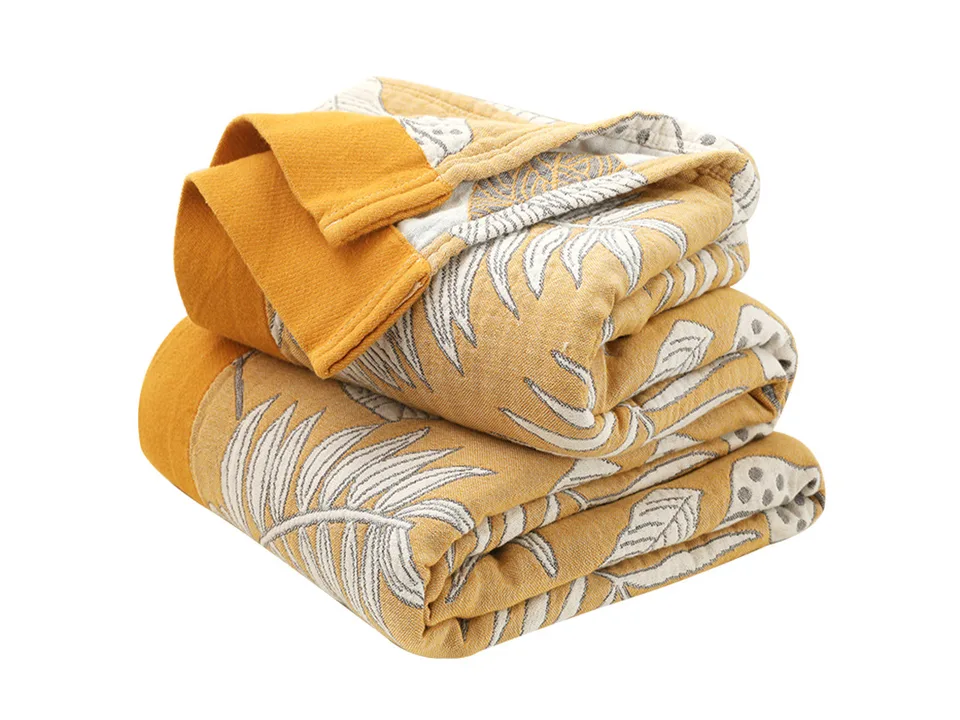 A folded yellow and white cotton blanket with a tropical leaf pattern.