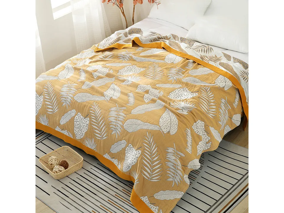 A yellow and white tropical leaf patterned blanket spread out on a bed.