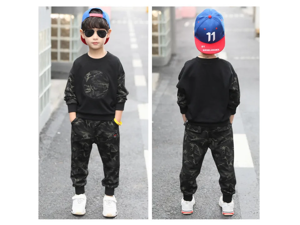 Front and back view of a boy wearing a black and camouflage two-piece outfit.